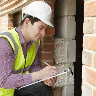 Inspector in a hard hat checking a brick wall